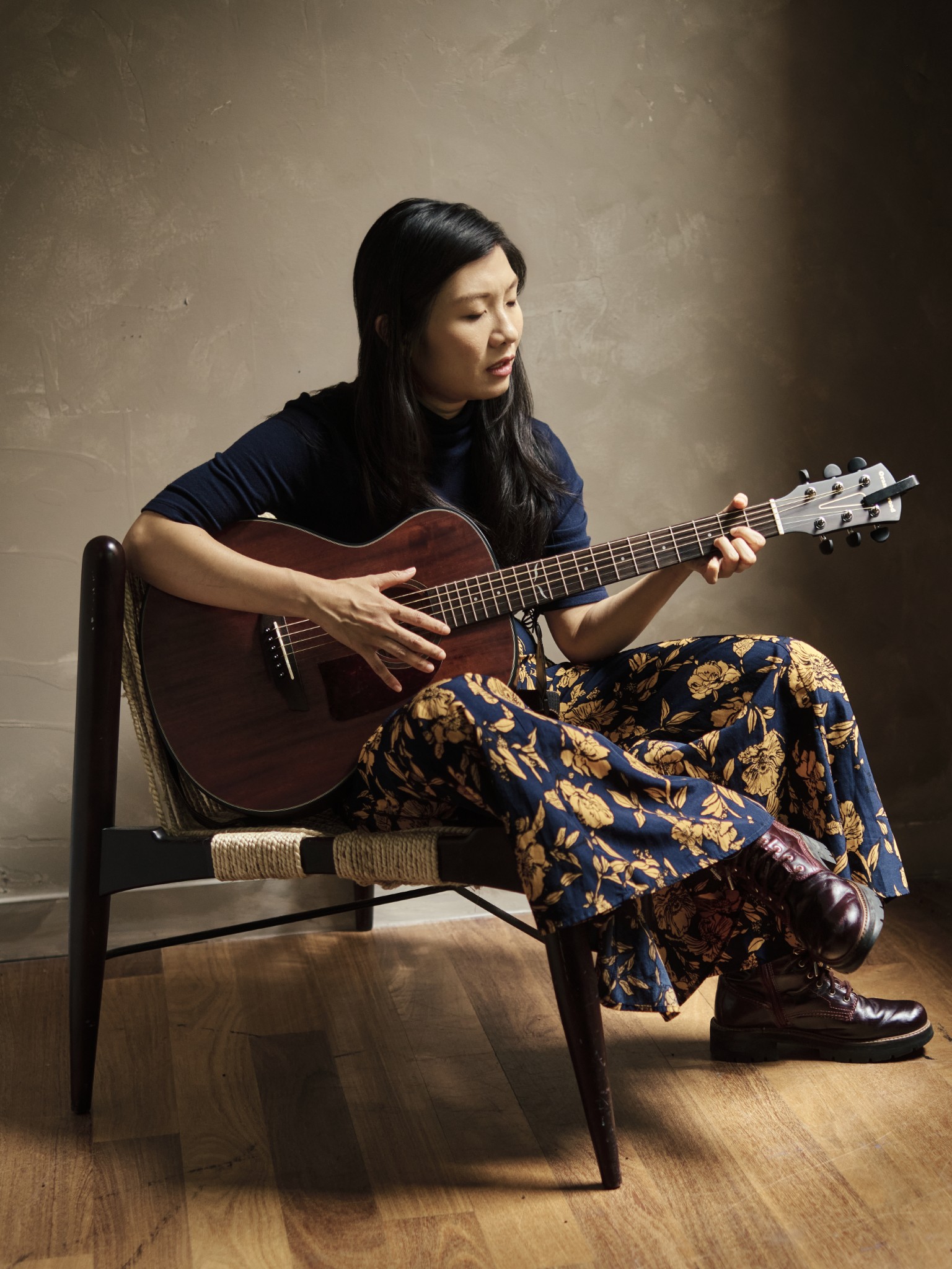 Musician seated with an acoustic guitar in a warmly lit interior.