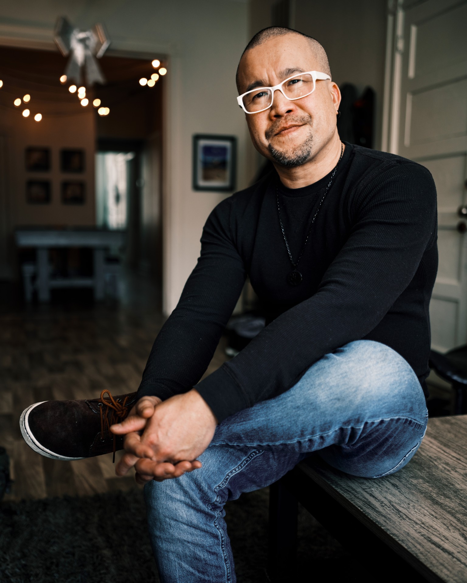 Man wearing white glasses seated casually in a creative workspace.